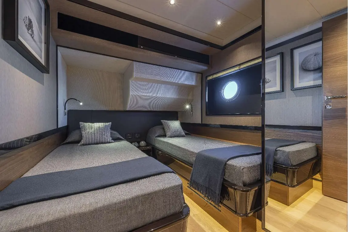 Modern cabin with two single beds, grey bedding, a round window, and framed artwork on walls, creating a stylish interior.
